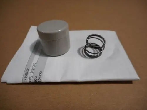 Graue Kunststoffkappe und ein metallener Spiraldichtring auf einem weißen Blatt Papier. Produkte von Remeha, geeignet für Anwendungen in Antriebswellen.